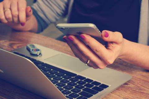 woman holding phone next to open laptop computer