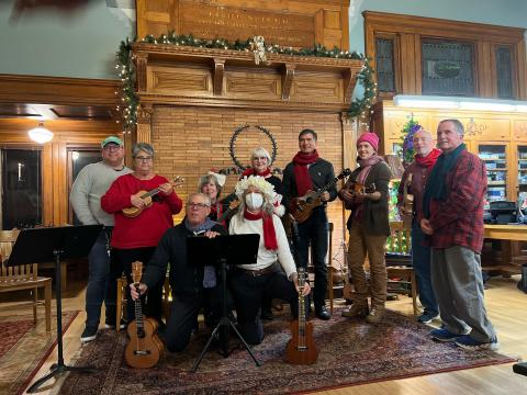 The Ukulele Strummers stand in front of the Mystic & Noank library's fireplace in the Spicer Reading Room.