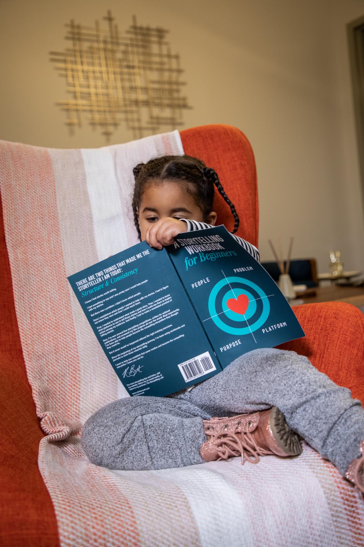 little girl sitting on a chair reading a book