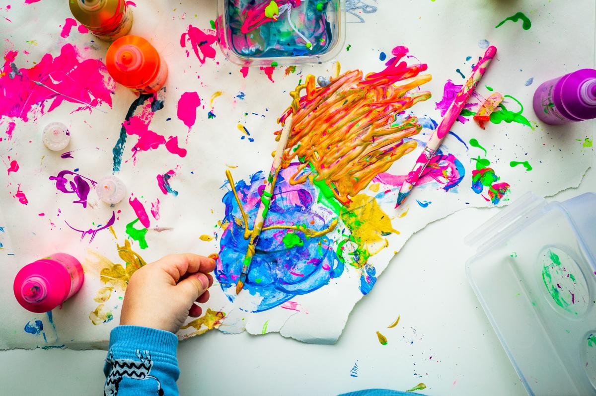 colorful paints on paper with child's hand reaching to crayola marker